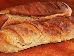 two loaves of fresh baked bread on wooden surface